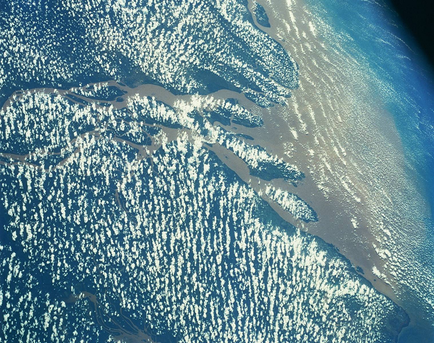 Color photograph of Earth from space, focusing on a cloudy area above rainforests.